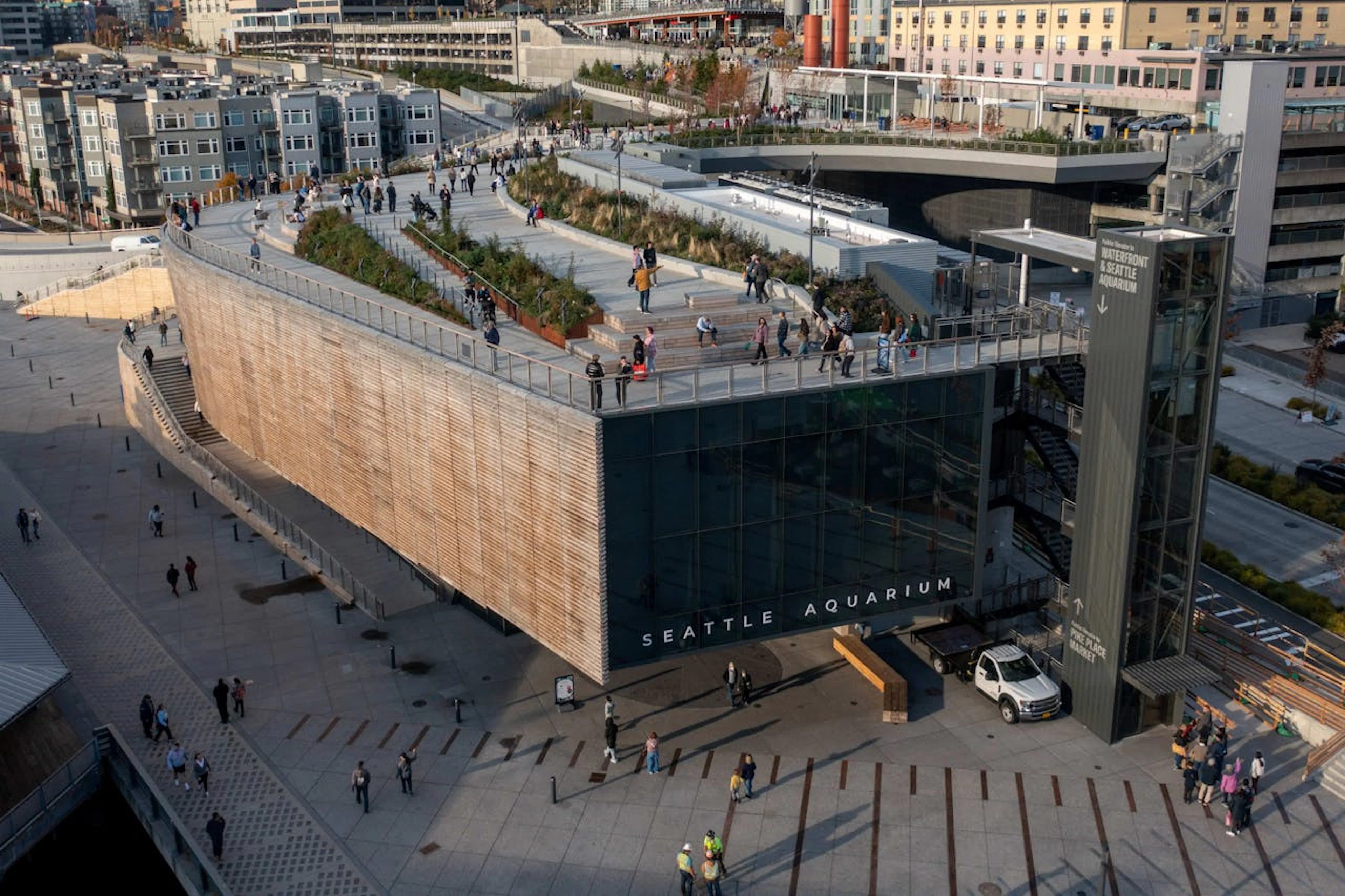 Seattle Aquarium entrance with visitors on the rooftop walkway and surrounding plaza.