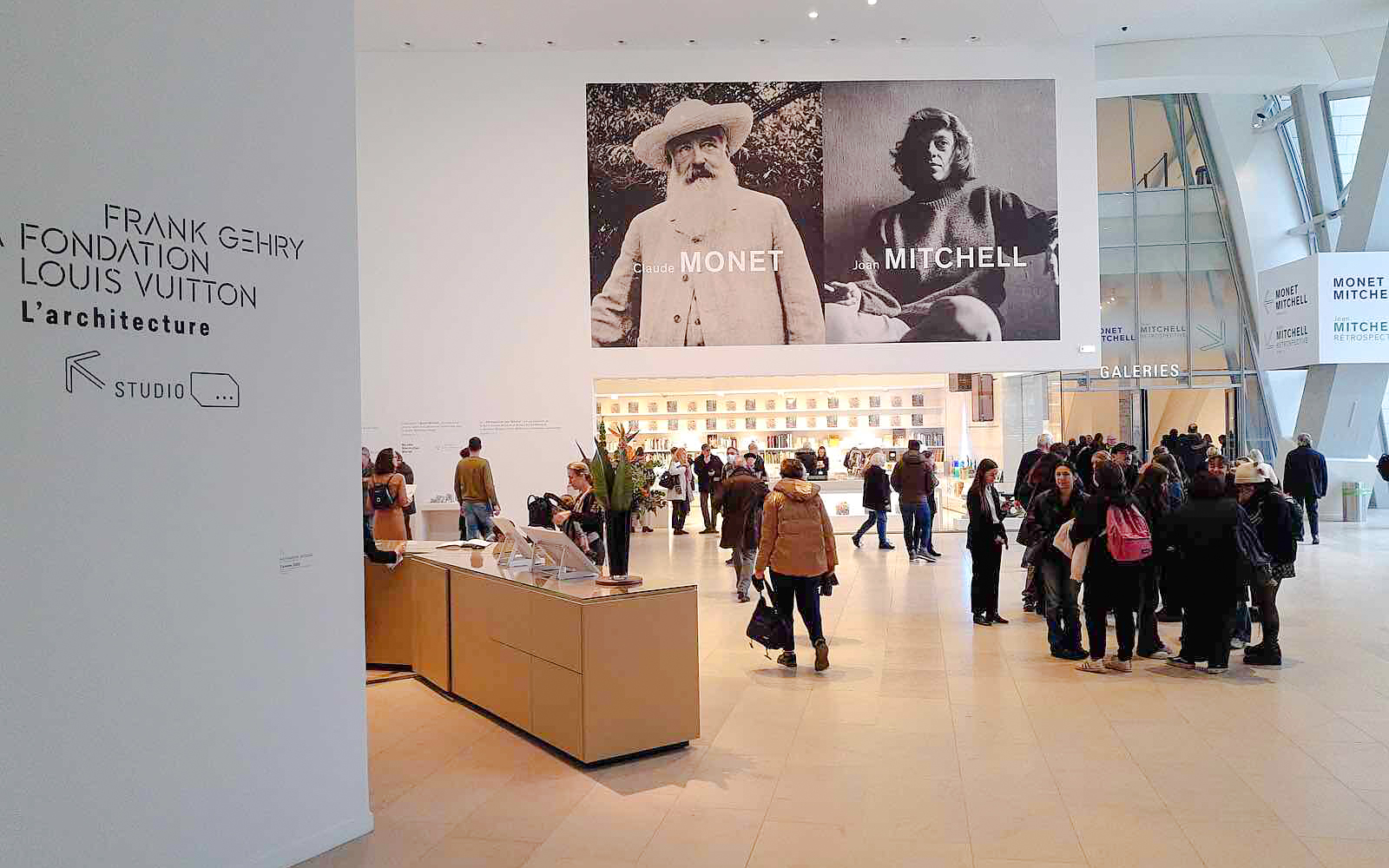 Interior of Louis Vuitton Foundation in Paris with visitors and Monet, Mitchell exhibition posters.