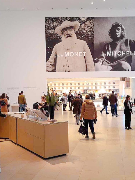Interior of Louis Vuitton Foundation in Paris with visitors and Monet, Mitchell exhibition posters.