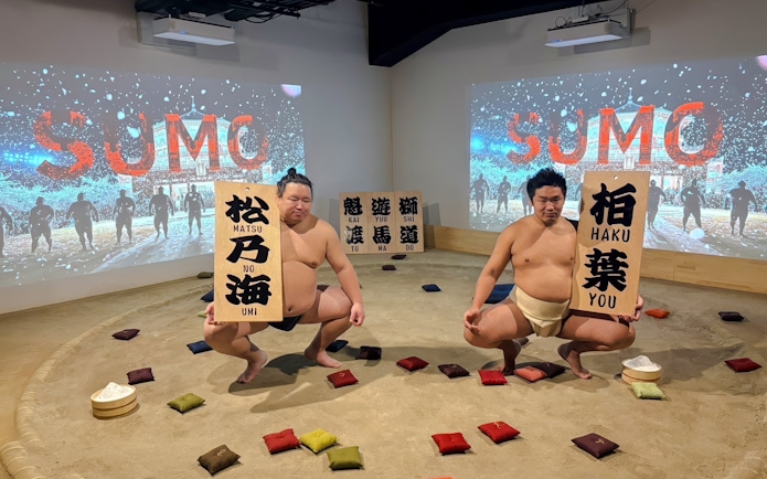 Sumo wrestlers performing at Ginza with souvenir signs in a sand ring.