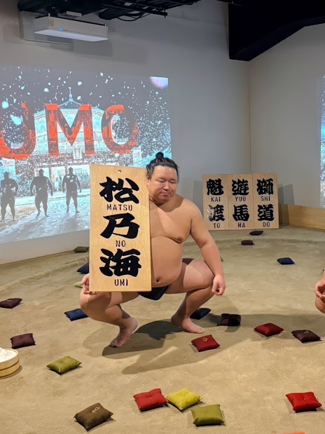 Sumo wrestlers performing at Ginza with souvenir signs in a sand ring.