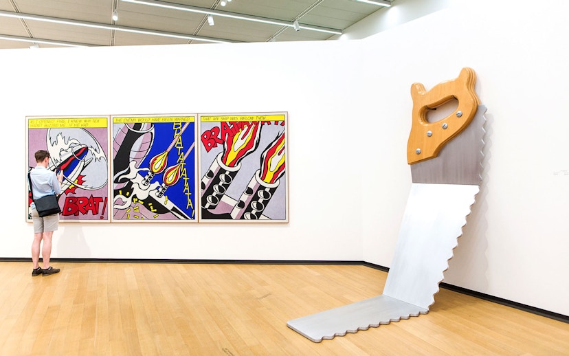 Visitor viewing pop art and large saw sculpture at Stedelijk Museum exhibits.