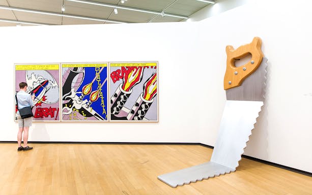 Visitor viewing pop art and large saw sculpture at Stedelijk Museum exhibits.