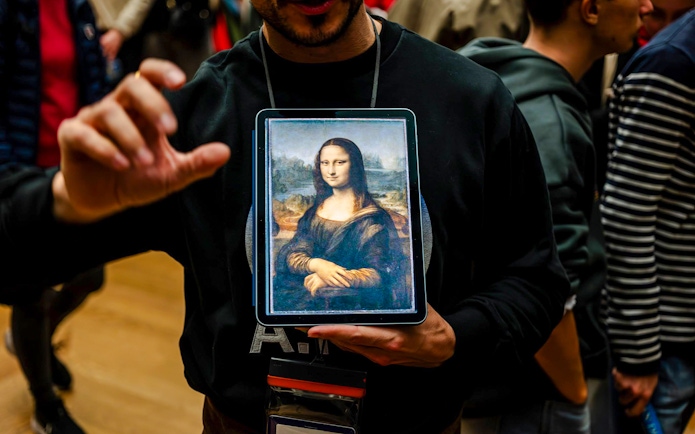 Guide showing Mona Lisa to tourists inside Louvre Museum, France.