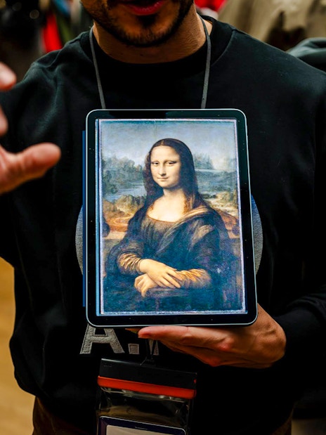 Guide showing Mona Lisa to tourists inside Louvre Museum, France.