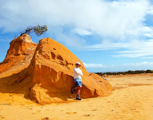 Person standing by a large limestone formation in the Pinnacles Desert, Western Australia.