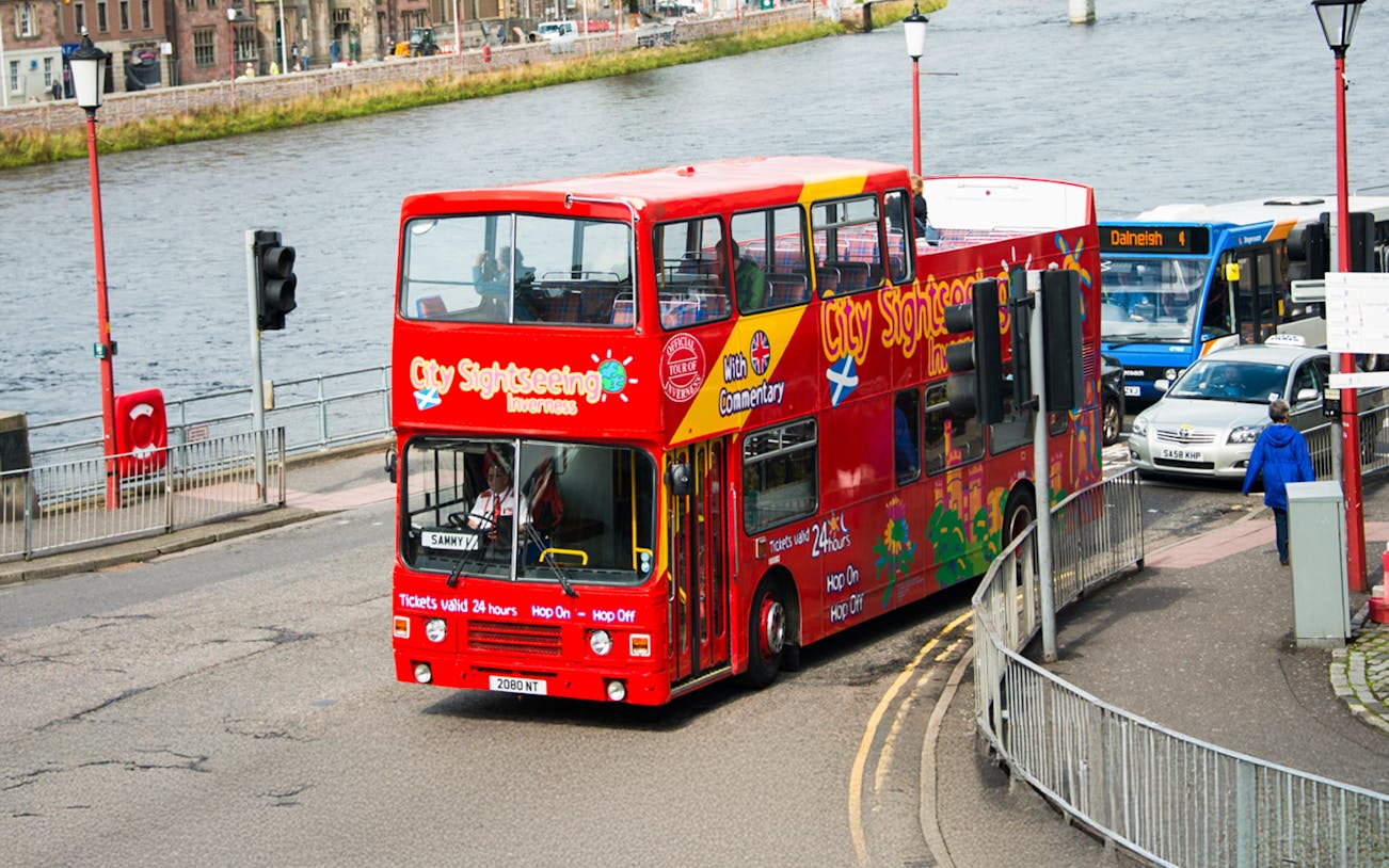 Red double-decker bus on Inverness hop-on hop-off tour by the river.