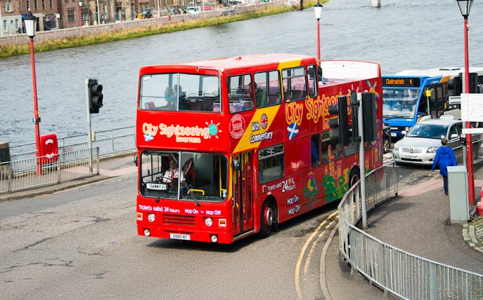 Red double-decker bus on Inverness hop-on hop-off tour by the river.