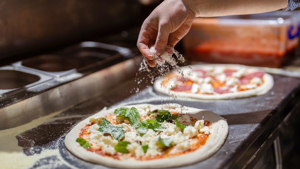 Hand sprinkling cheese on pizza during cooking class.