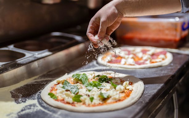 Hand sprinkling cheese on pizza during cooking class.