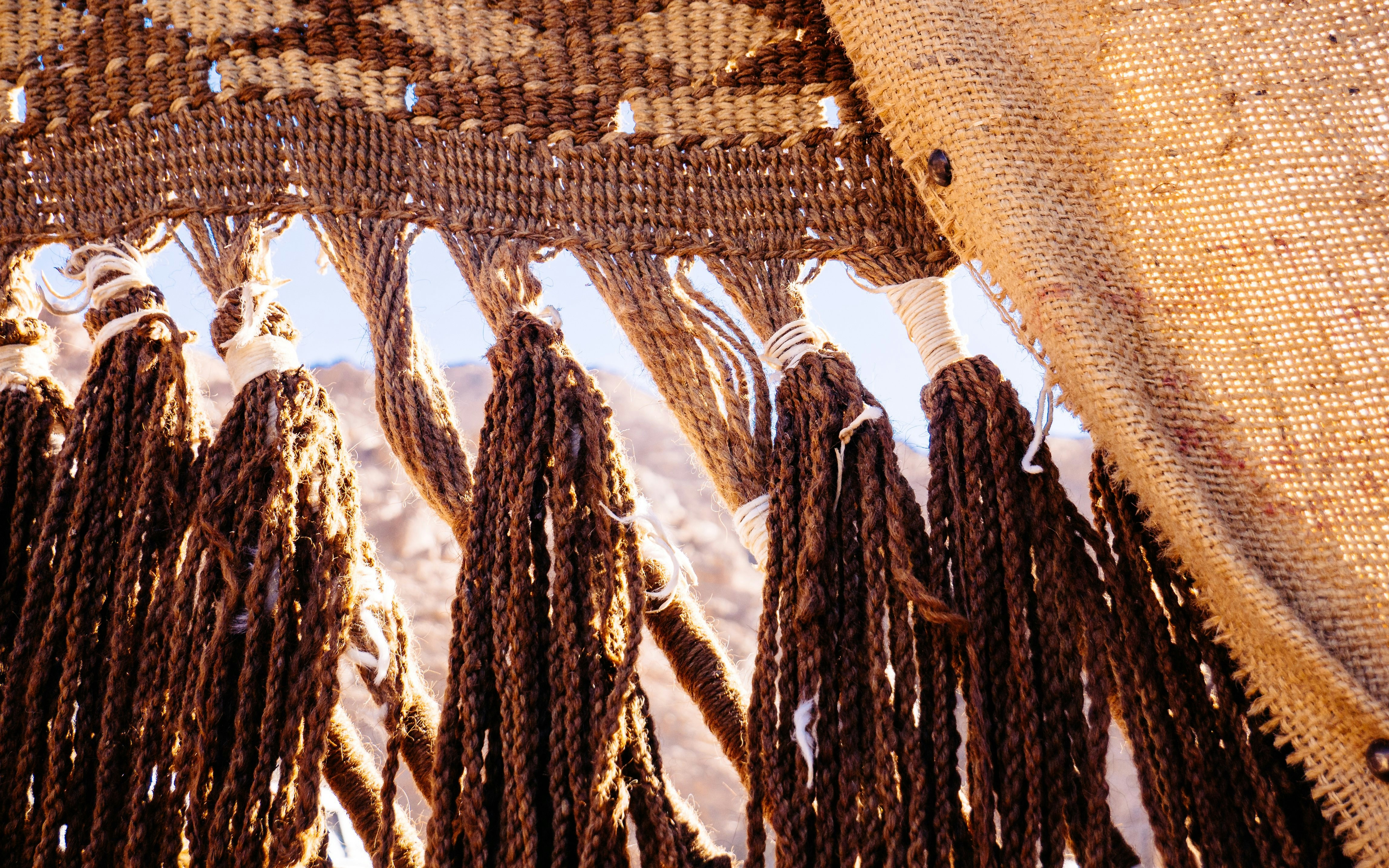 Traditional jute Bedouin tent with woven patterns and tassels in desert setting.
