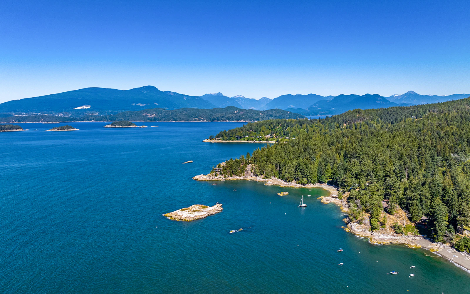 Bowen Island aerial view with forested coastline and sailboat during Vancouver seaplane tour.
