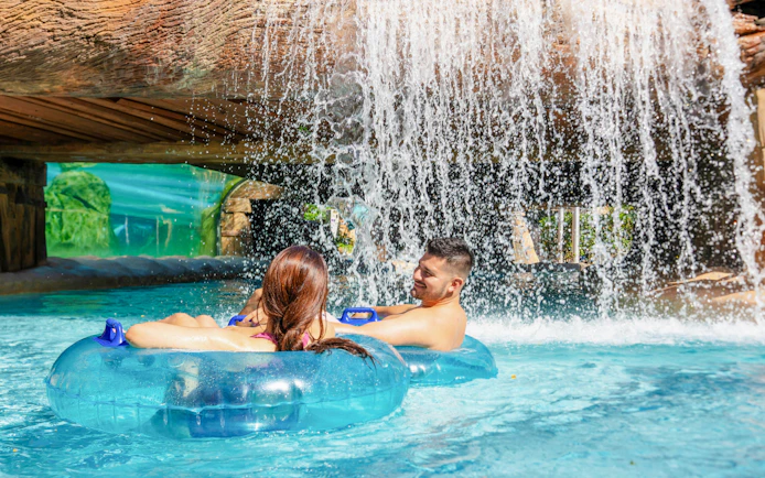 Couple floating on inner tubes under waterfall at Aquatica Orlando.