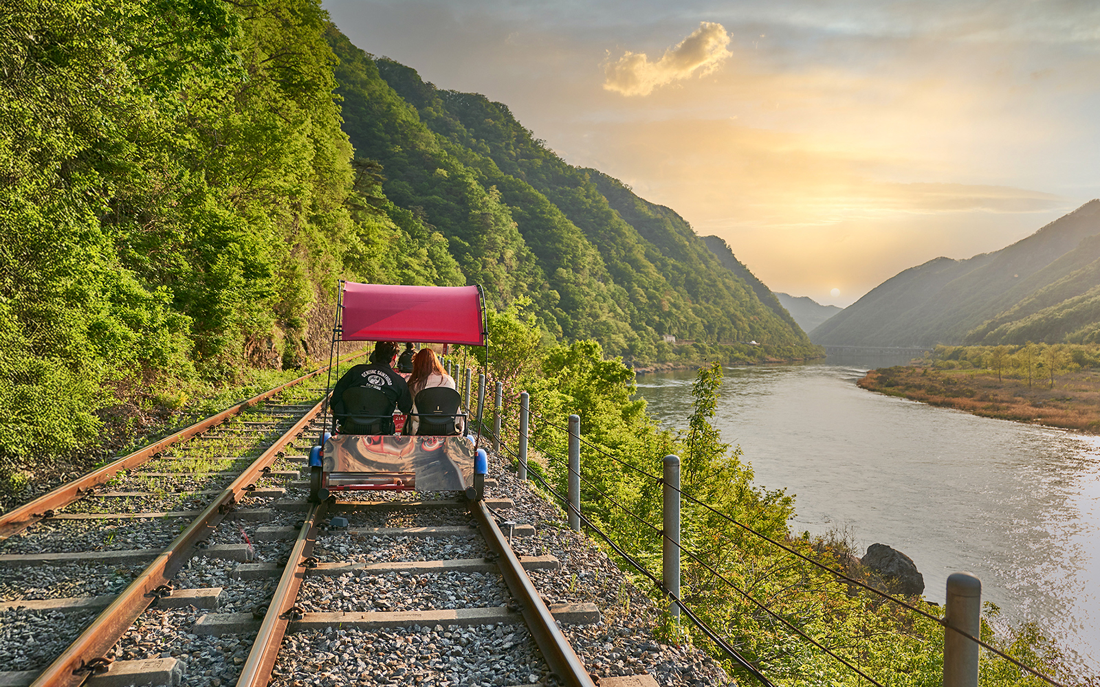Couple on Gangchon Rail Bike along river track at sunset, South Korea.