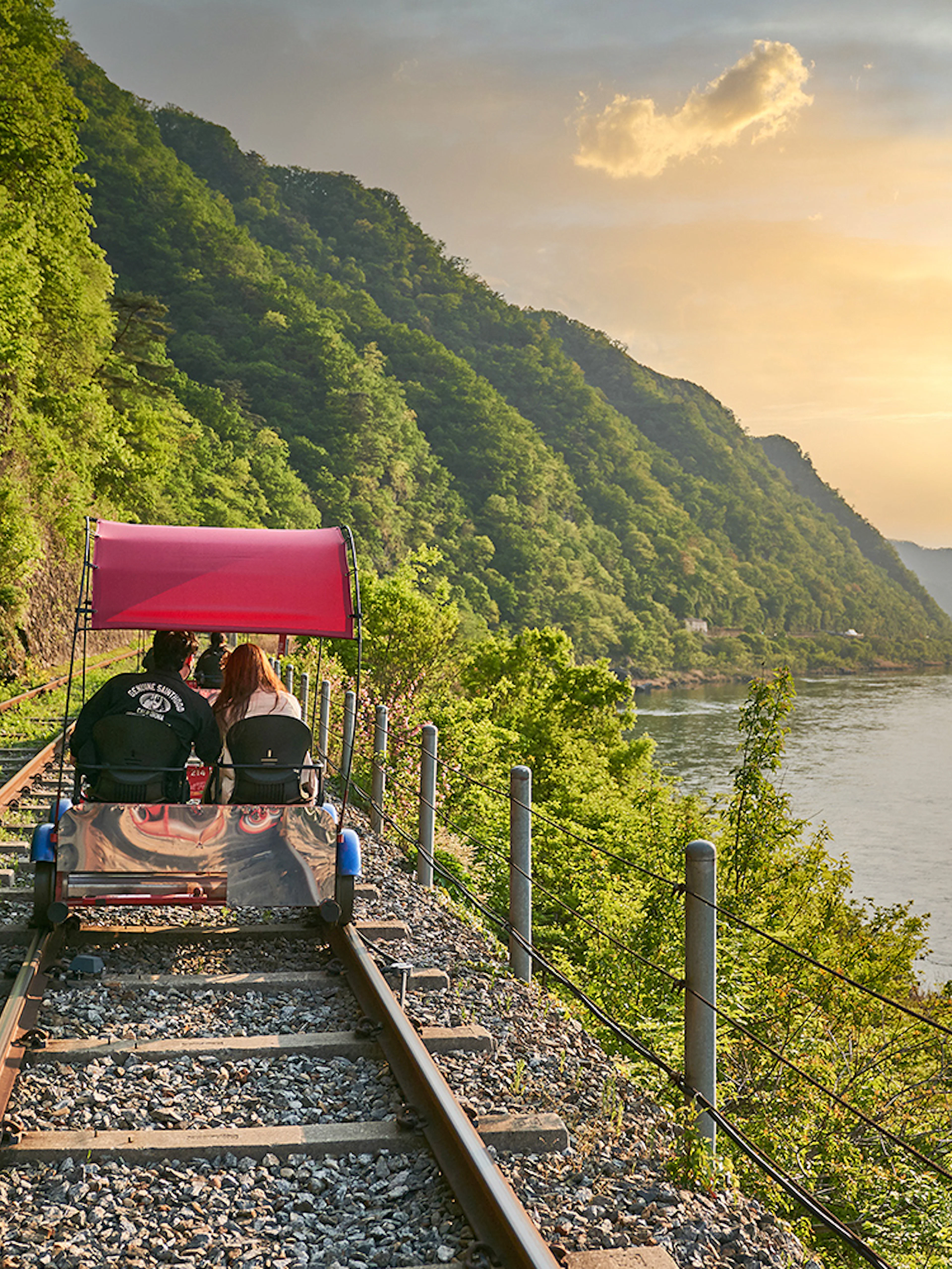 Couple on Gangchon Rail Bike along river track at sunset, South Korea.