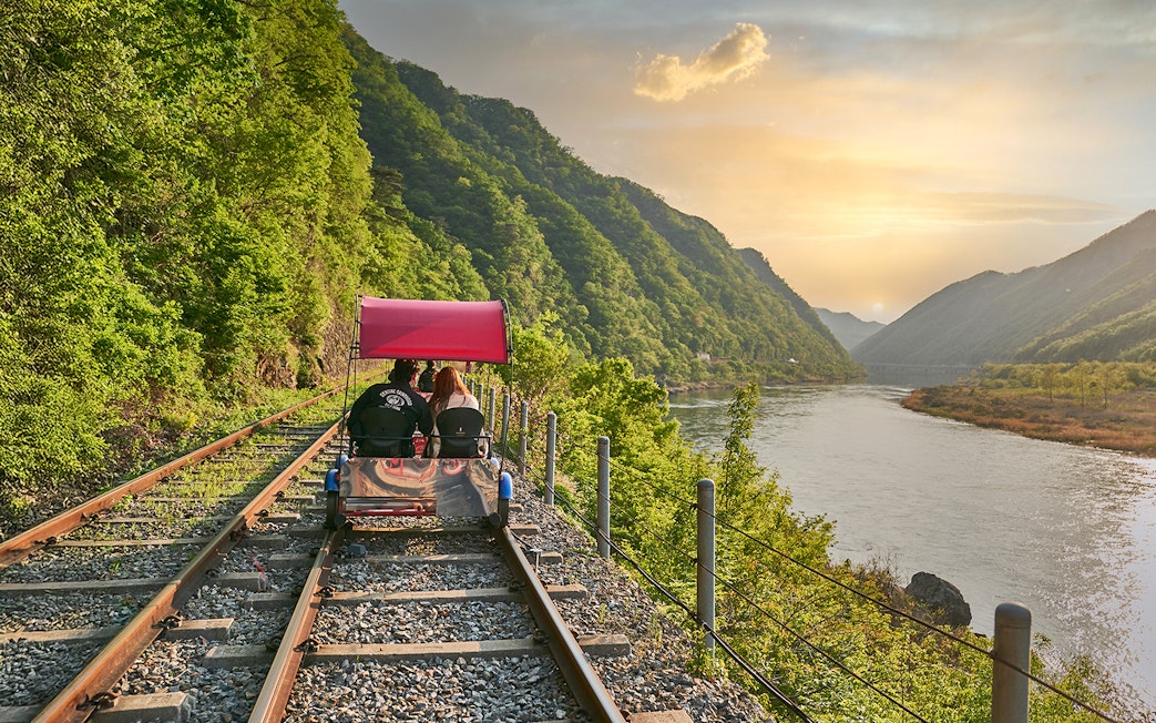 Couple on Gangchon Rail Bike along river track at sunset, South Korea.