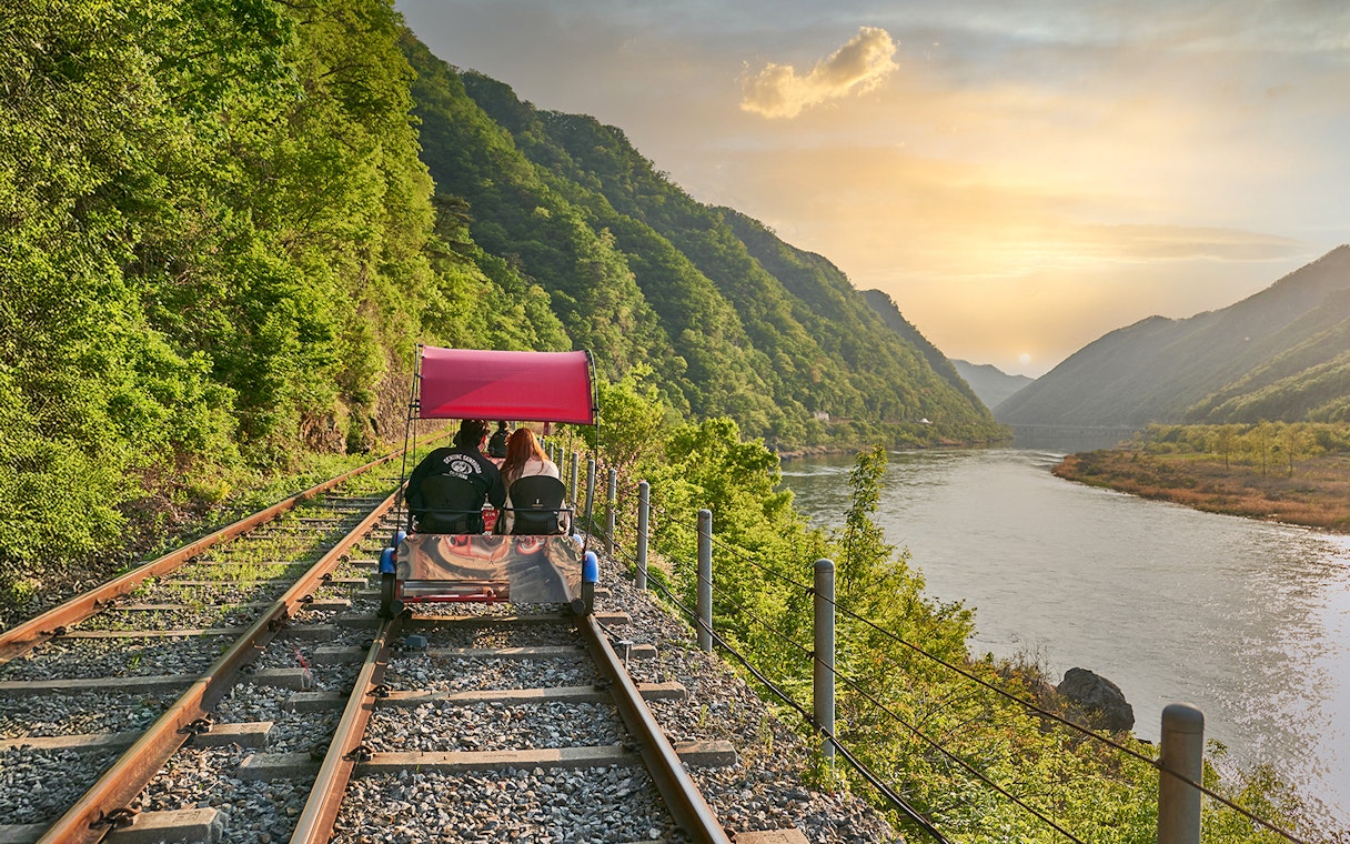 Couple on Gangchon Rail Bike along river track at sunset, South Korea.