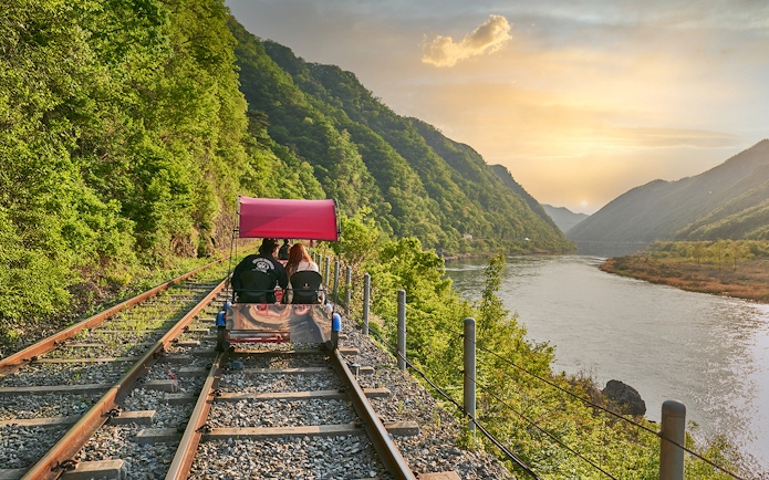 Couple on Gangchon Rail Bike along river track at sunset, South Korea.