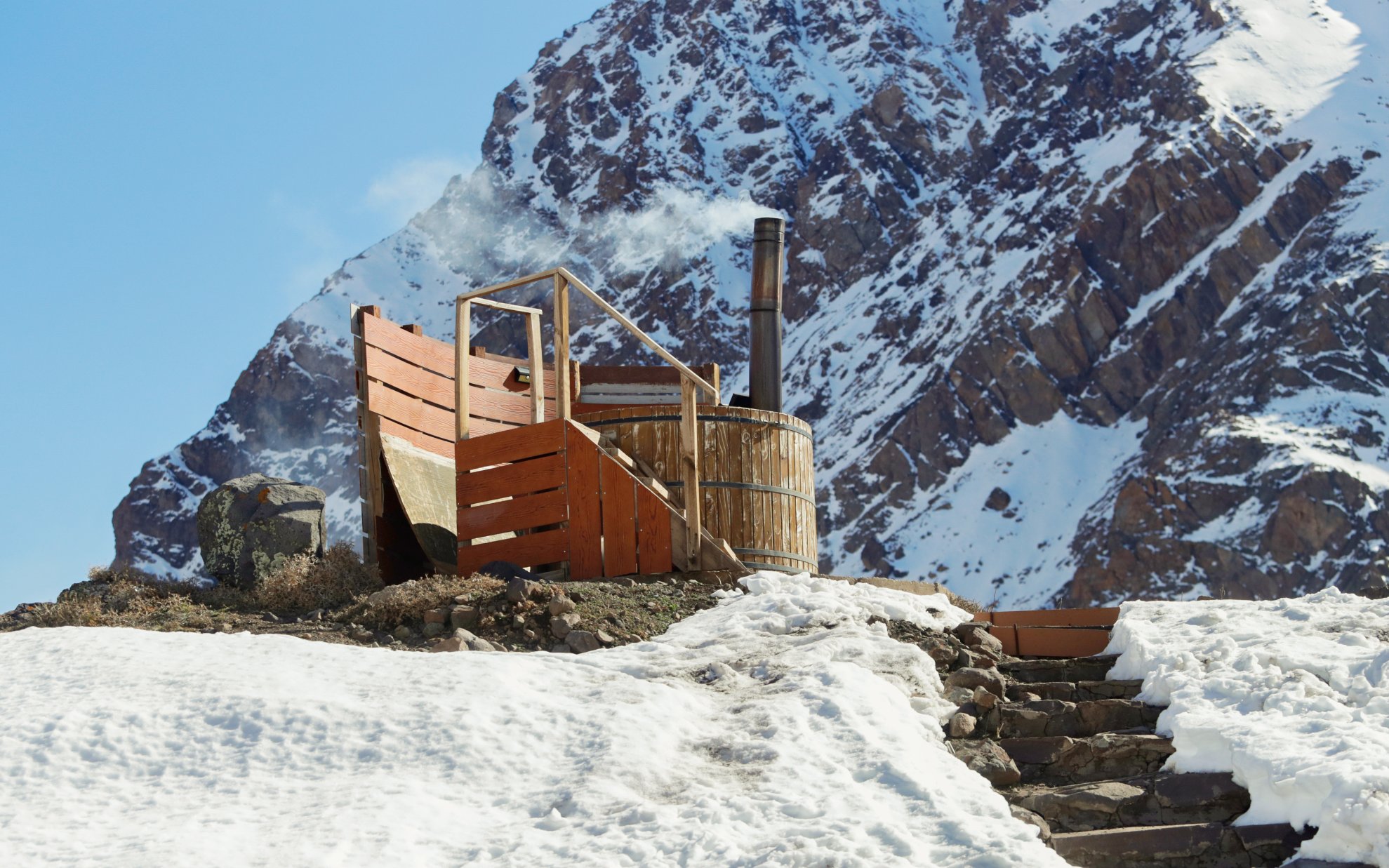 Wooden hot tub at Lodge El Morado with snowy mountain backdrop.