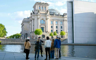 Group on guided tour outside Reichstag building, Berlin, near river.
