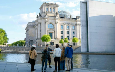 Group on guided tour outside Reichstag building, Berlin, near river.