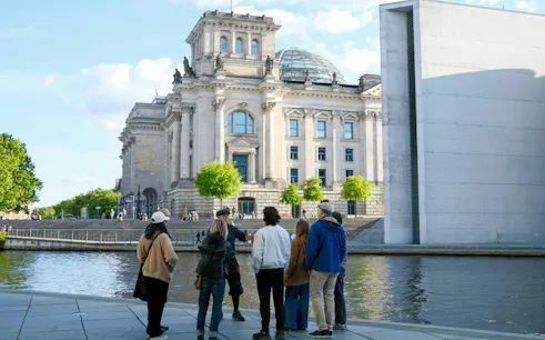 Group on guided tour outside Reichstag building, Berlin, near river.