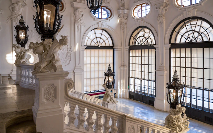 Upper Belvedere Palace interior staircase with ornate sculptures and large windows, Vienna.