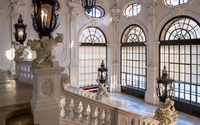 Upper Belvedere Palace interior staircase with ornate sculptures and large windows, Vienna.