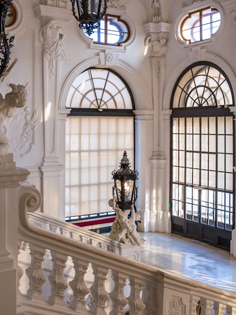 Upper Belvedere Palace interior staircase with ornate sculptures and large windows, Vienna.