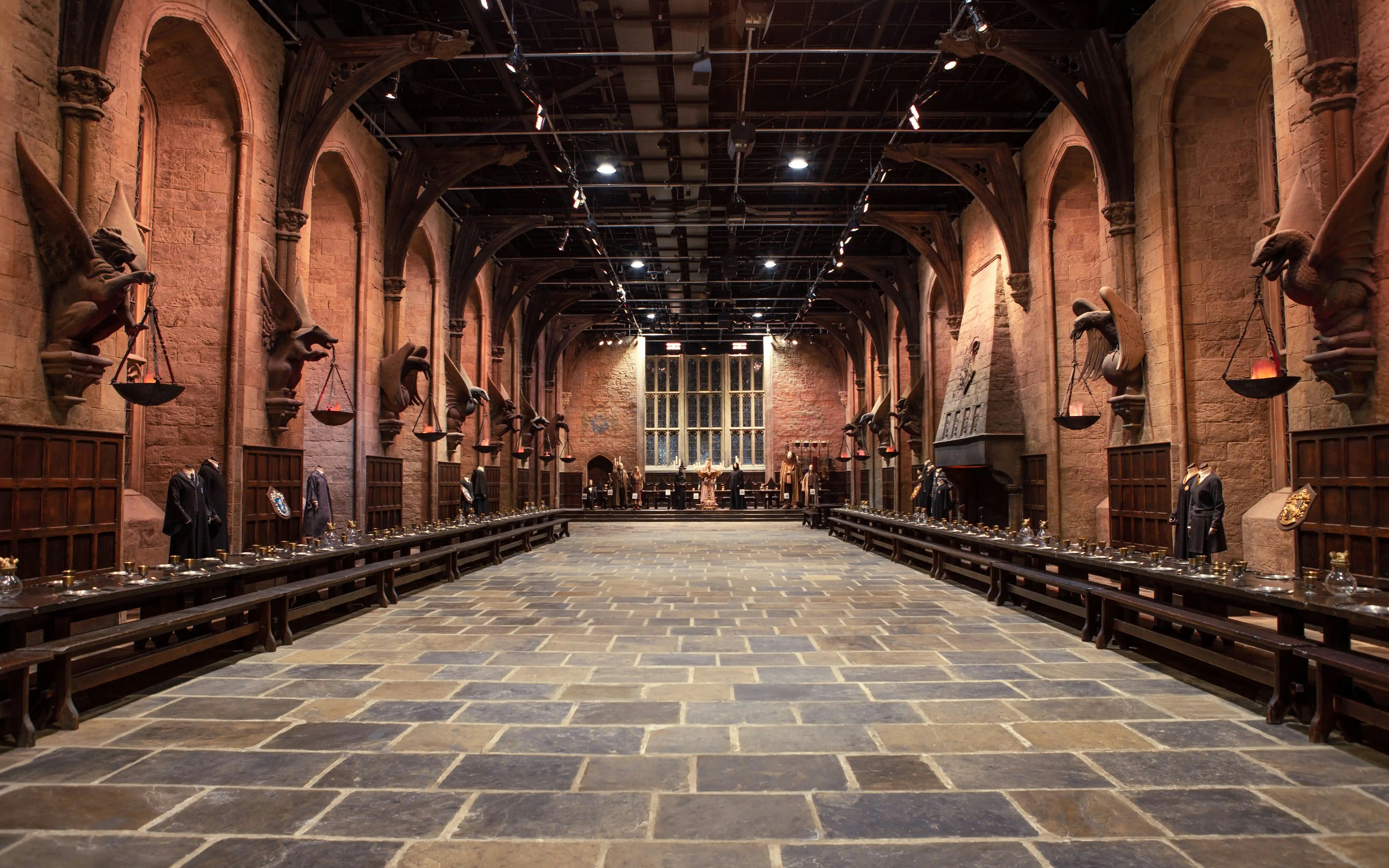 Great Hall at Harry Potter™ Warner Bros. Studio, long tables, stone arches, and costumes displayed.