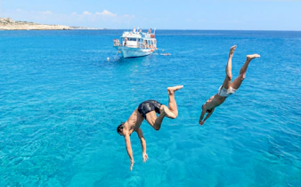 Two people diving into clear blue water near a boat on the Blue Lagoon Cruise, Protaras.