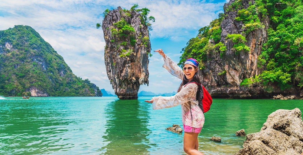 Woman posing at James Bond Island, Thailand, with limestone cliffs and turquoise water in the background.