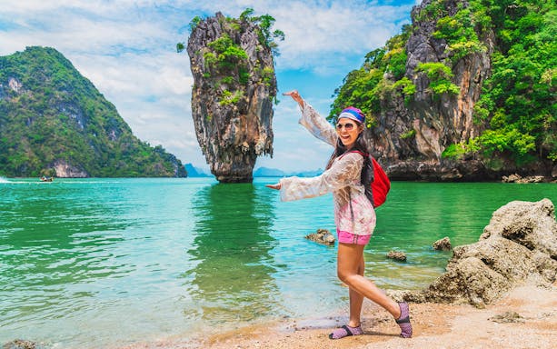 Woman posing at James Bond Island, Thailand, with limestone cliffs and turquoise water in the background.