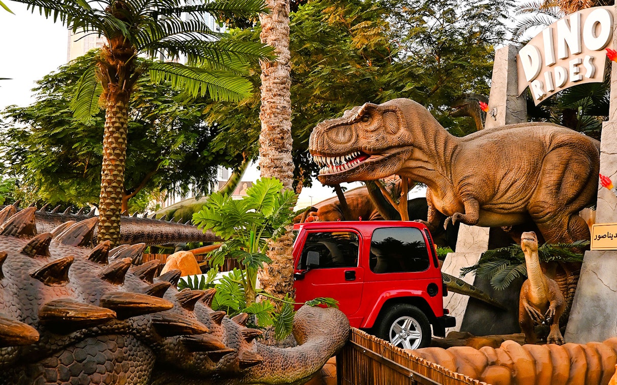 Dinosaur sculptures and red jeep at Dino Rides, Dubai Garden Glow.