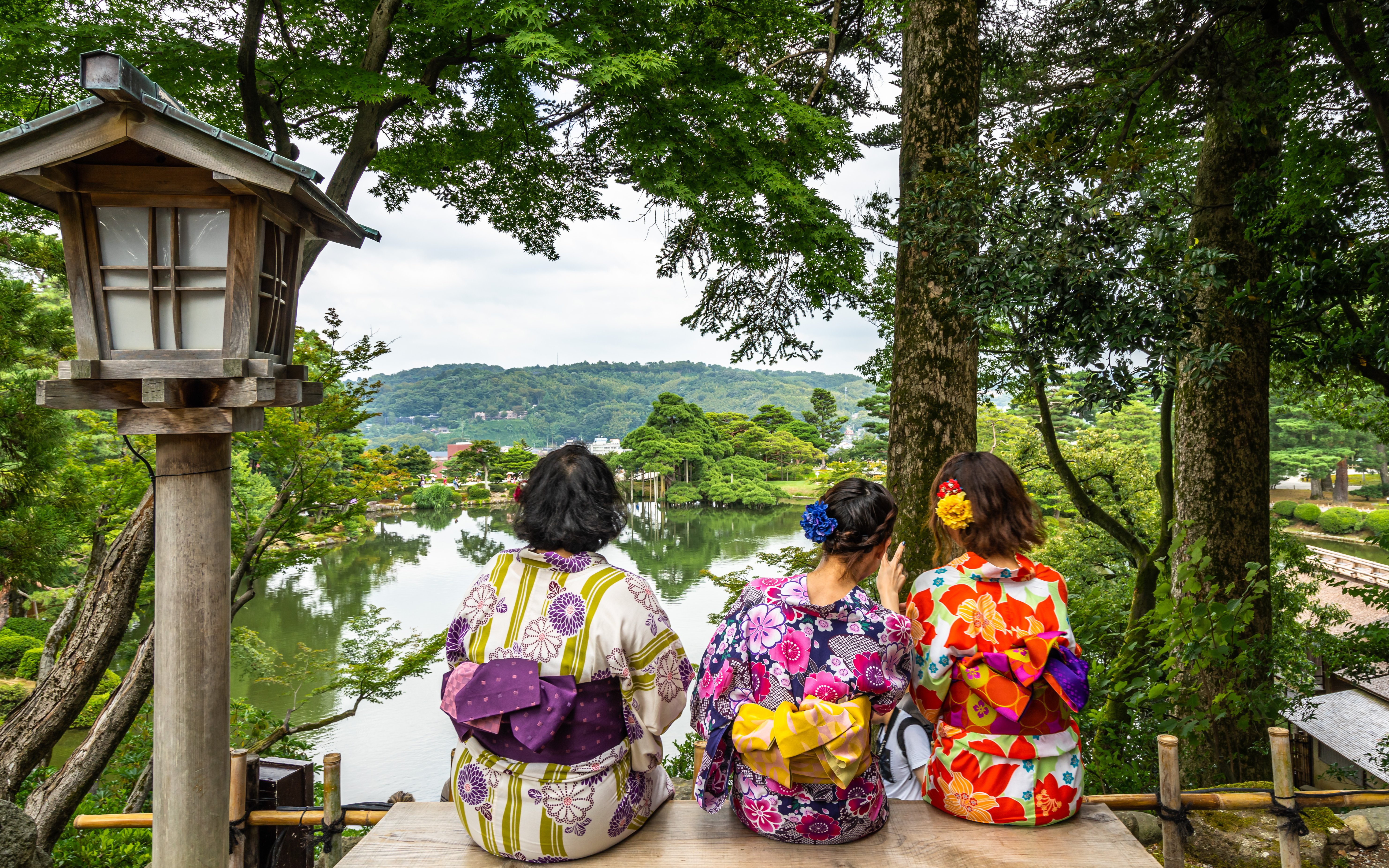 Women in kimonos sitting on a bench overlooking Kenrokuen Garden, Kanazawa, Japan.