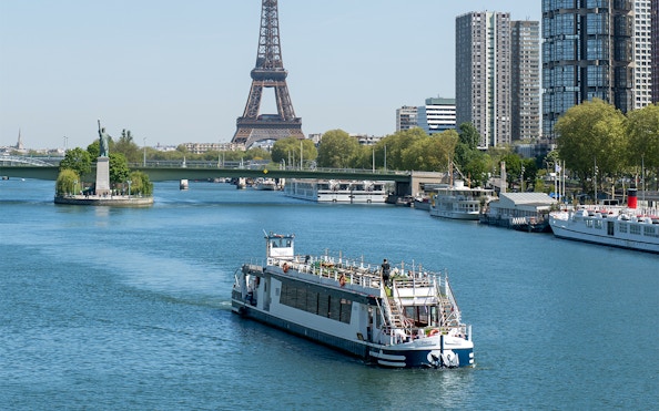 Cruise boat on the Seine River with Eiffel Tower and Paris skyline in the background.