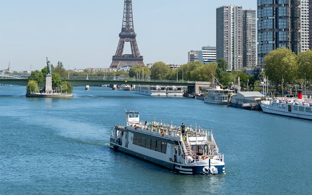 Cruise boat on the Seine River with Eiffel Tower and Paris skyline in the background.