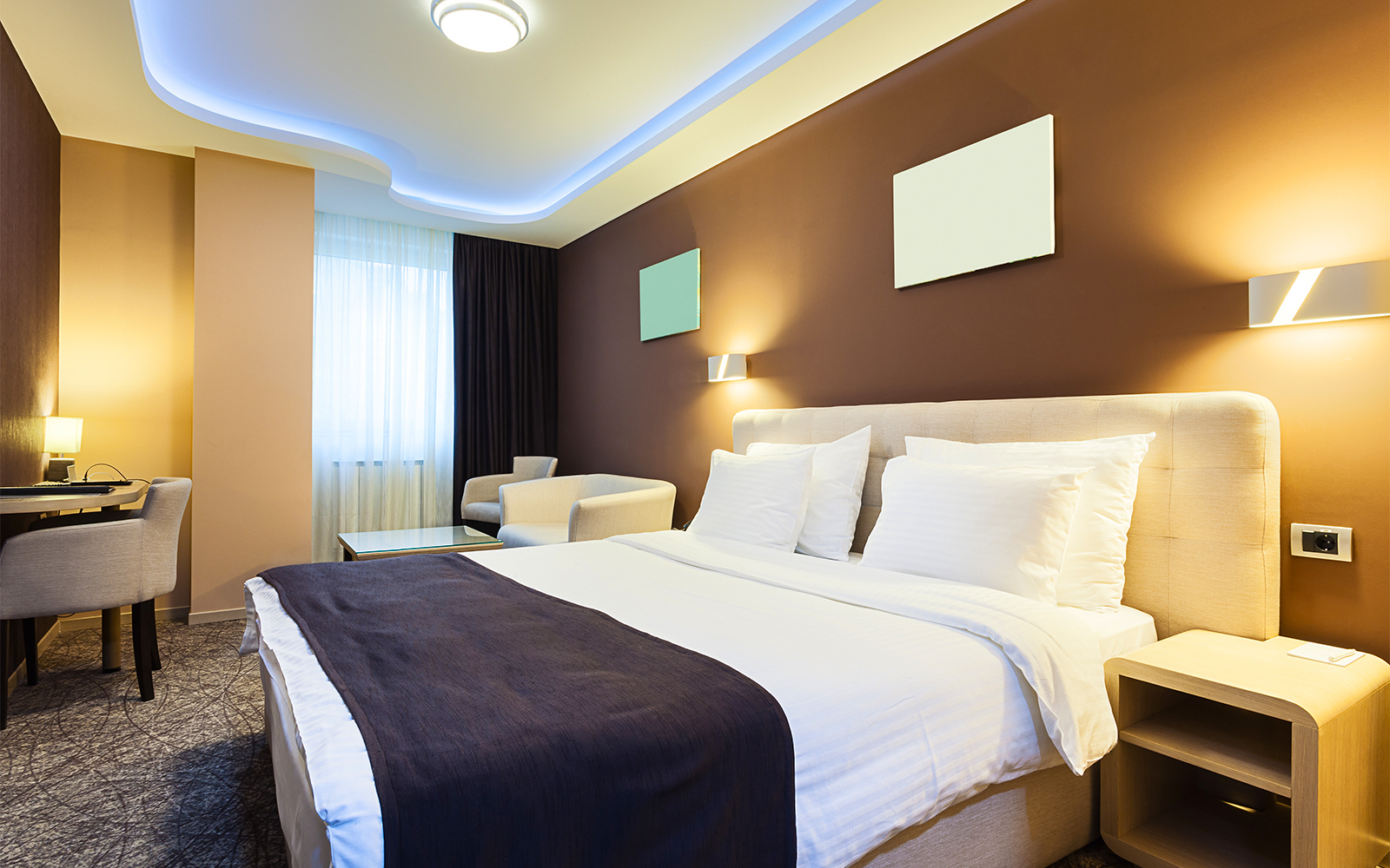Modern hotel room with double bed, desk, and city view through large window.