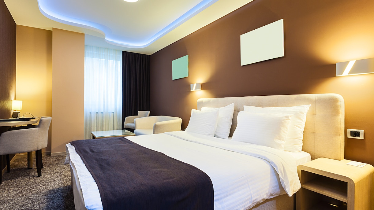 Modern hotel room with double bed, desk, and city view through large window.