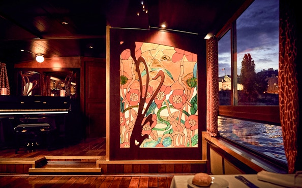Stained glass art and piano inside Maxim's Seine River cruise boat at sunset.
