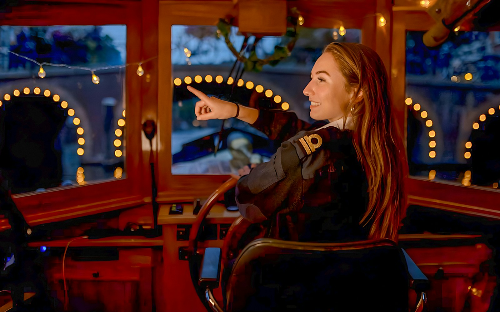 Skipper steering boat during Amsterdam Light Festival Cruise, pointing at illuminated canal bridge.