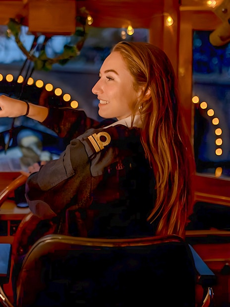Skipper steering boat during Amsterdam Light Festival Cruise, pointing at illuminated canal bridge.