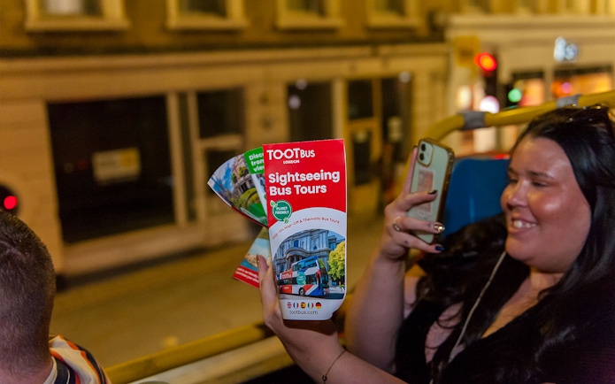 Sightseeing bus tour brochure held by a person on a night tour in London.