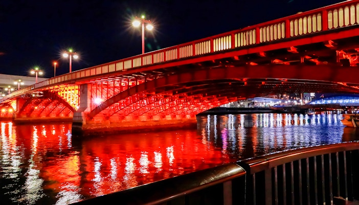 Azuma Bridge illuminated at night, reflecting on the Sumida River in Tokyo.