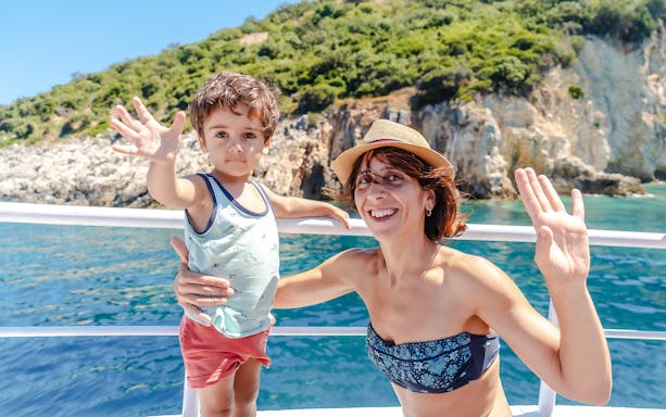 Mother and son waving on a boat near Gremina Beach, Albania.