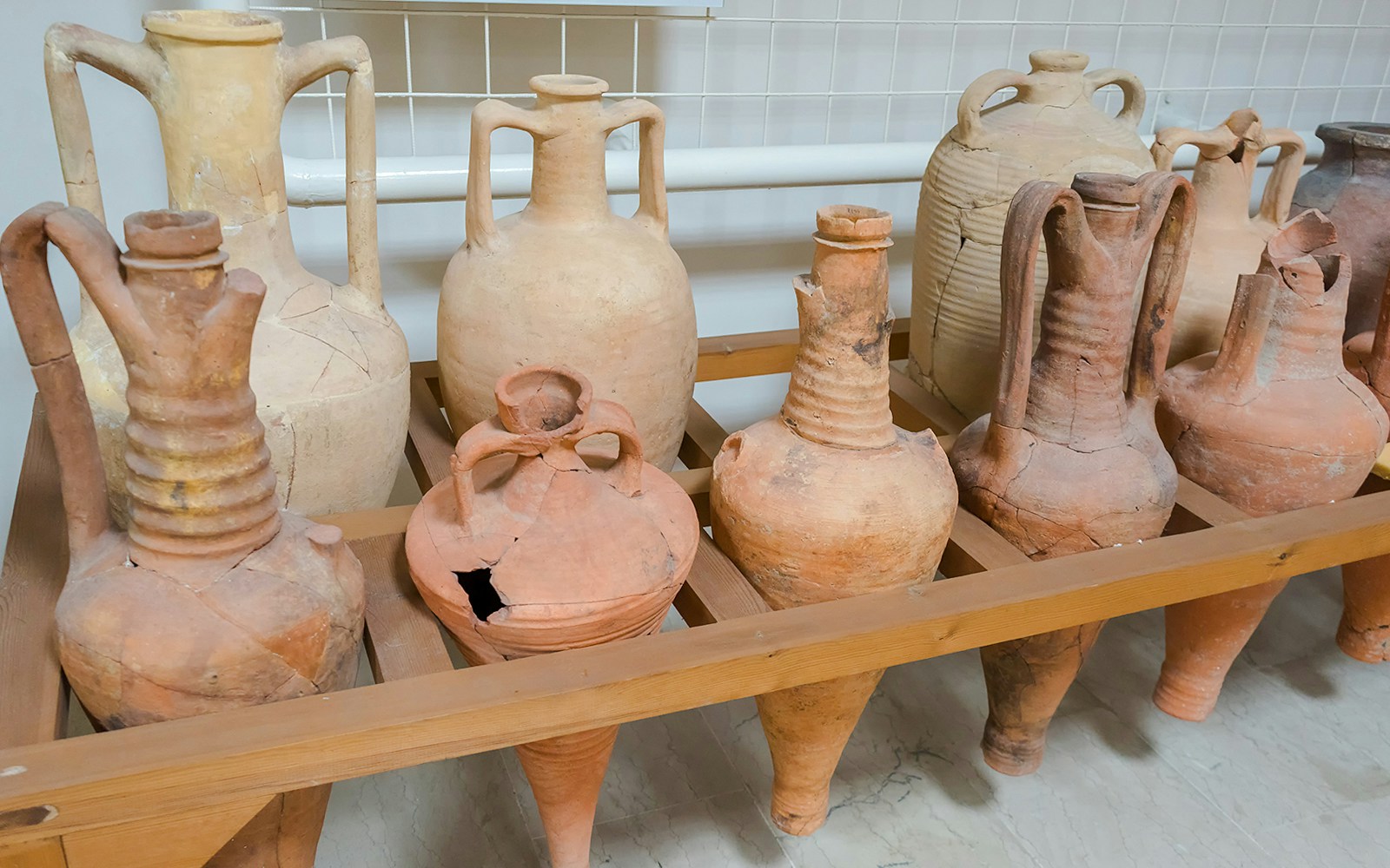 Antique Greek clay jugs displayed on a wooden shelf.