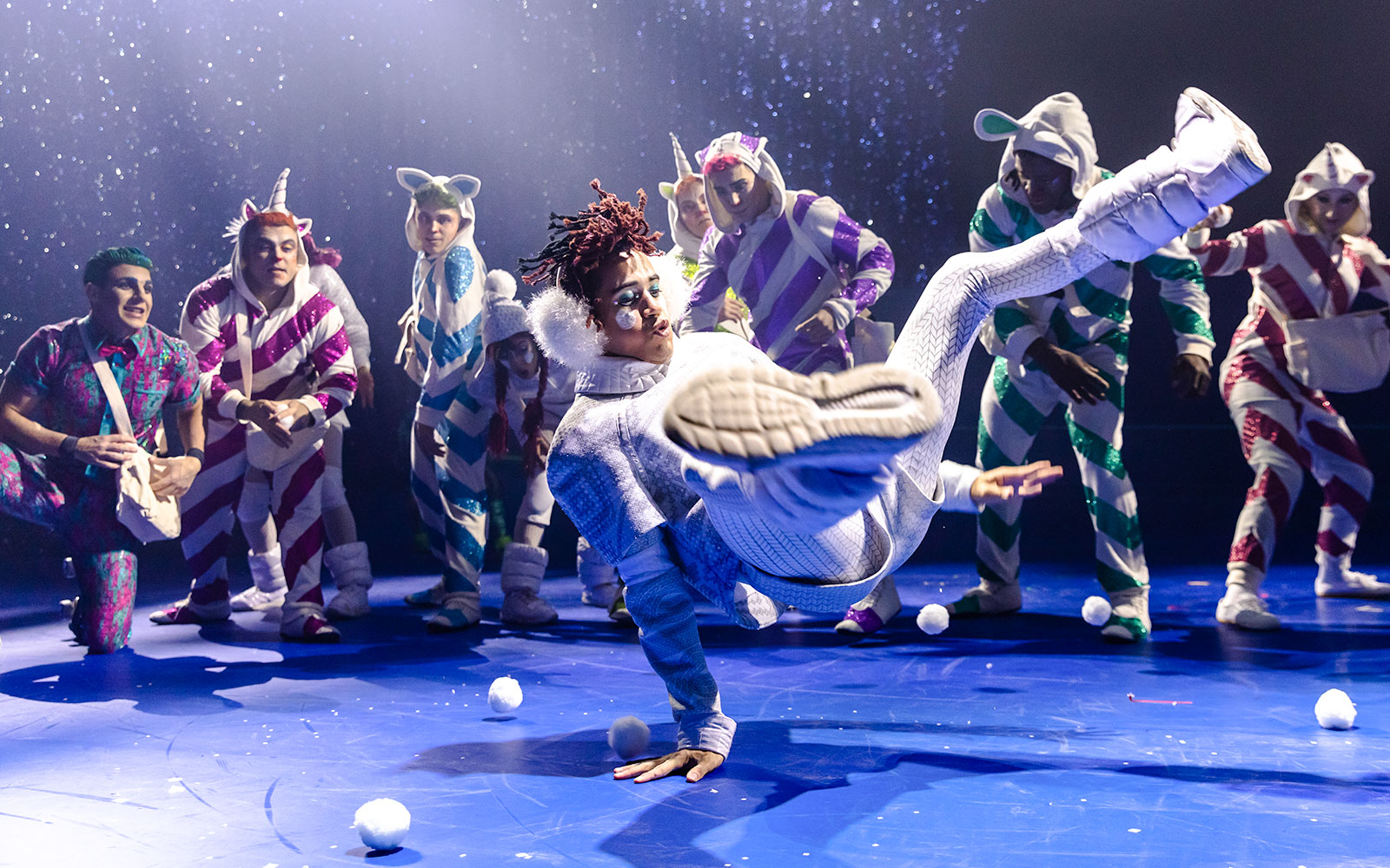 Performer breakdancing in Cirque du Soleil 'Twas The Night Before show with colorful costumed dancers.