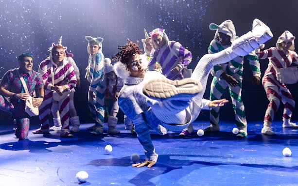 Performer breakdancing in Cirque du Soleil 'Twas The Night Before show with colorful costumed dancers.