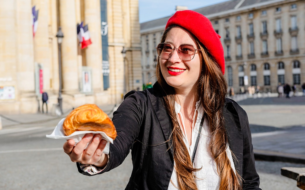 Woman in red beret offering croissant on Emily in Paris Locations Walking Tour.