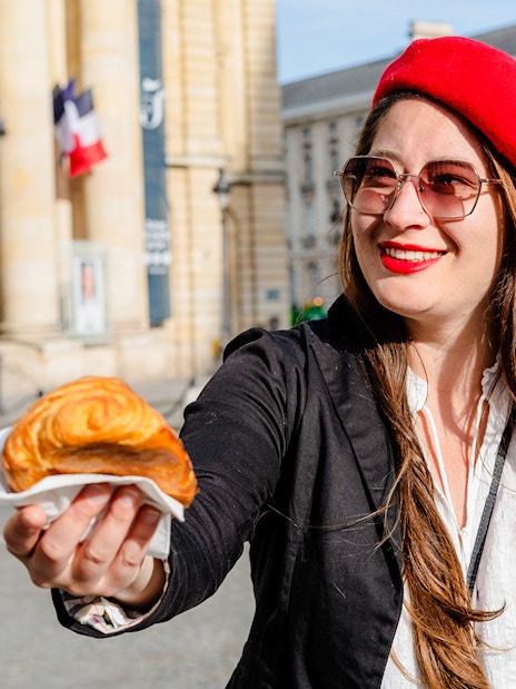 Woman in red beret offering croissant on Emily in Paris Locations Walking Tour.